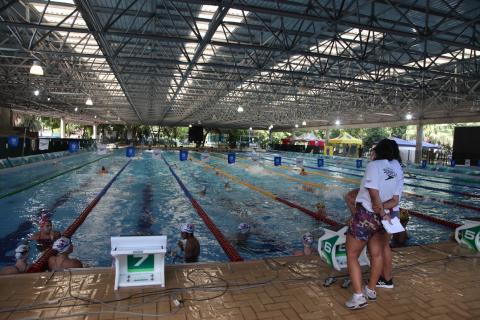 Vista geral da piscina olímpica, com alguns atletas na cabeceira. #Paratodosverem