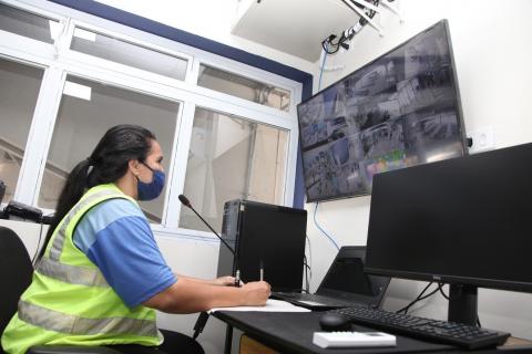 Mulher está sozinha em sala. Diante dela uma tela grande de monitoramento. #Paratodosverem