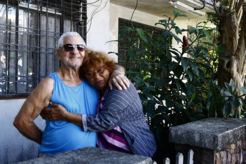 Leonita posa para foto abraçada com um senhor de óculso escuros na frente da casa