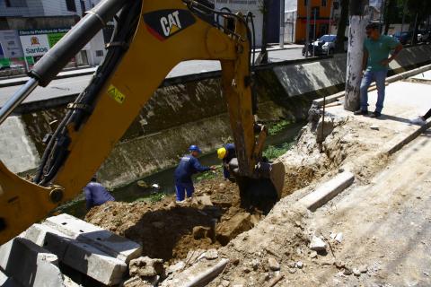 operários e máquina trabalham em borda de canal #pracegover 