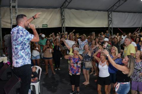 Cantor, em cima do palco, anima público que canta e dança na pista. #pracegover