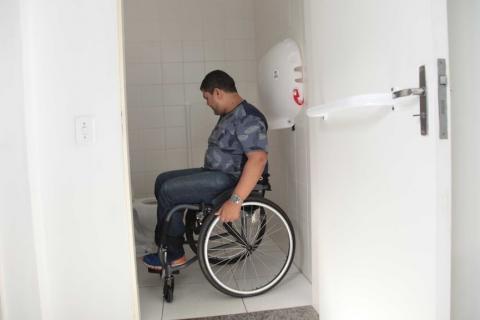 Banheiro com porta na dimensão adequada para cadeirante e suportes de segurança. #Pracegover