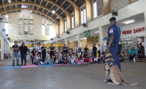 guarda está parado com a cadela na frente das crianças, sentadas #pracegover 