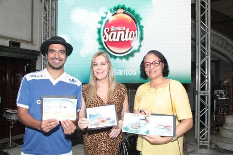 Artistas plásticos seguram seus diplomas à frente de banner do Ilumina Santos. #Pracegover