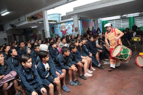 homem toca bumbo e passa na frente de estudantes #pracegover 