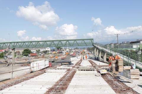 Vista geral da obra do viaduto da Alemoa, com homens trabalhando e passarela lateral. #Paratodosverem