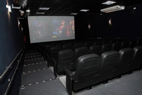 Sala de cinema vazia, com poltronas escuras e telão ao fundo. #Pracegover