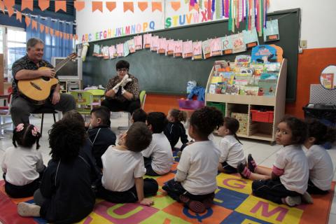 Crianças sentadas sobre tapete acompanham apresentação de músico. #Pracegover