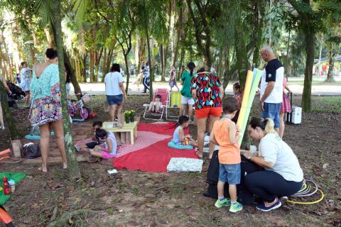 Crianças e adultos estão se divertindo em uma área verde. #Pracegover