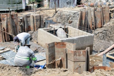 homens abaixados atuando ao lado de caixa de concreto #paratodosverem 