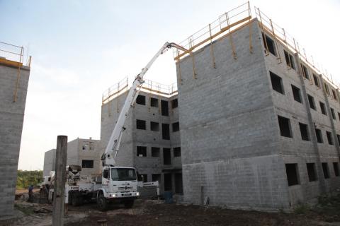 Caminhão com braço basculante ao lado de prédio em construção. #Paratodosverem