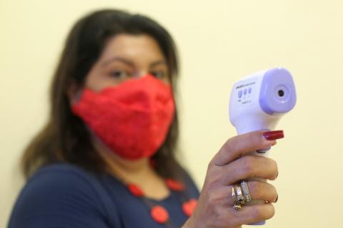 Mulher usando máscara aponta termômetro para a foto. #paratodosverem