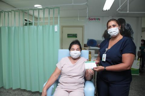 Mulher vacinada exibe certificado de vacinação ao lado da mulher que aplicou a vacina. #Paratodosverem