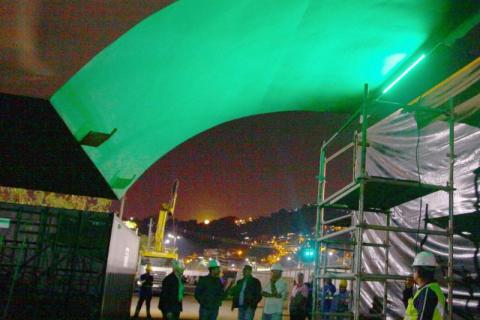 Viaduto é iluminado na cor verde, com operários e gestores abaixo. #pracegover