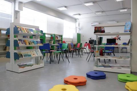 Biblioteca com estantes, cadeiras e almofadas coloridas no chão. #pracegover