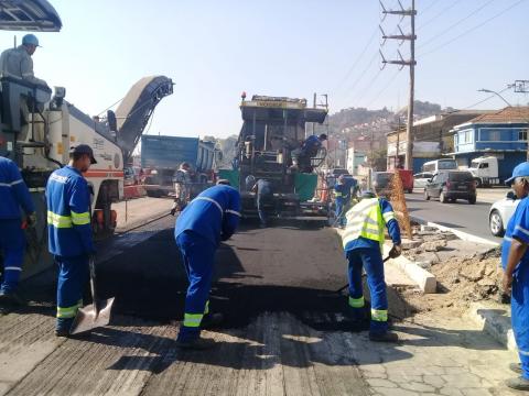 Quatro homens uniformizados aplicam asfalto em parte da via
