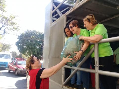 Mulher entrega sacola com roupas para três mulheres de verde sobre caminhão