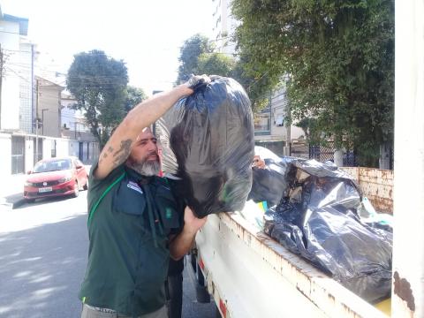 Homem despeja sacola com roupa sobre caçamba de caminhão