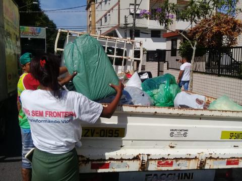 Mulher com uniforma da ONG Sem Fronteiras despeja sacola com roupa sobre caçamba de caminhão