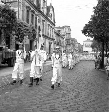 Antigo desfile no Centro de Santos, com homens da Marinha carregando bandeiras. #Pracegover