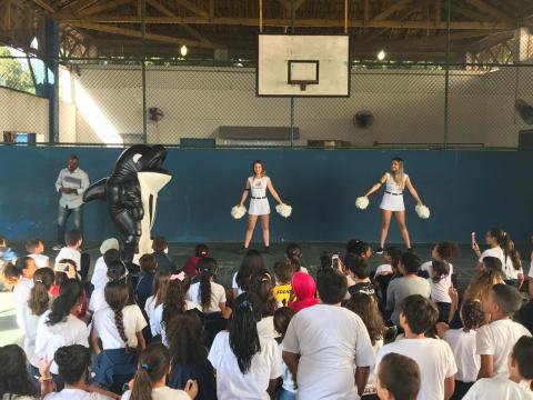 mascote e animadoras de torcida se apresentam para alunos sentados em frente #pracegover 