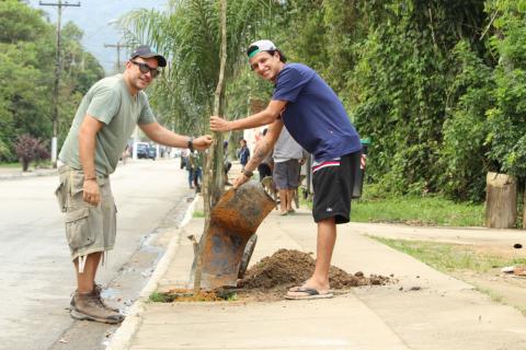 dois rapazes plantam muda em calçada #pracegover