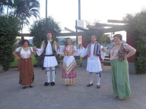 Grupo de dança grega em frente a arcos inspirados na cultura daquele país