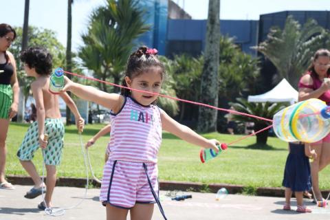 Menina abre os braços ao esticar brinquedo feito de elástico e garrafas PET