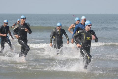 #pracegover Sete homens com uniforme de natação deixam o mar correndo