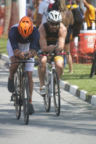 #pracegover na avenida da praia, dois homens pedalam com uniforme e capacete