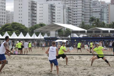 #pracegover Duas duplas de homens praticam tênis quadra de areia na praia