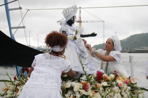 #pracegover Em frente ao mar, duar mulheres de branco ajeitam estátua de Iemanjá