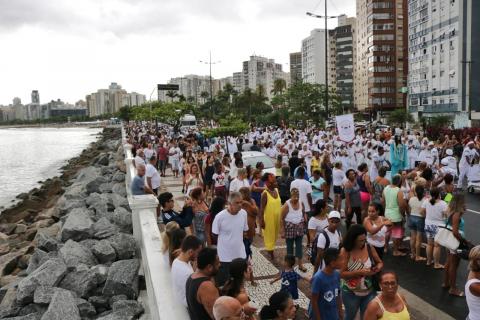 #pracegover Centenas de epssoas caminham em procissão pelo calçadão da orla da Ponta da Praia