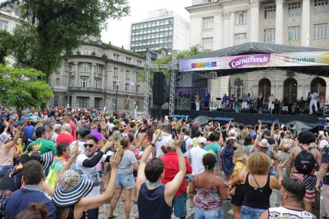 #pracegover De costas para a foto, público ergue os braços durante apresentação musical no palco