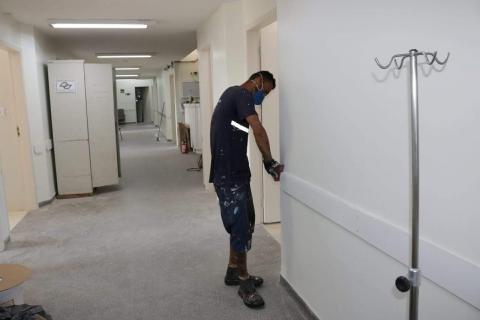 Homem está lixando parede em corredor hospitalar. #Paratodosverem 