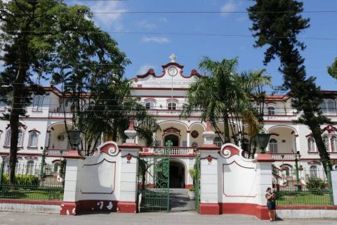 Fachada da Beneficência Portuguesa, com árvores no jardim e portão semi-aberto. #Paratodosverem