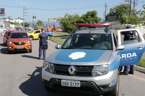 Agente da Guarda, ao fundo, se aproxima de veículo. Em primeiro plano há uma viatura da guarda municipal. #Paratodosverem