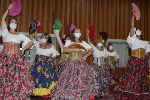 Mulheres fazem coreografia usando saias longas e leques nas mãos. todas estão usando máscaras faciais. #Paratodosverem