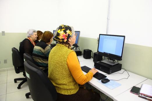 Mulheres idosas estão sentadas diante de desktops. #Paratodosverem