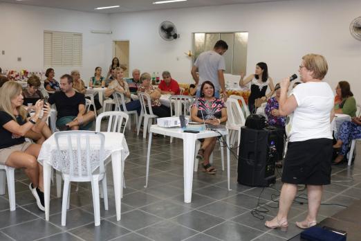 idosa fala ao microfone enquanto pessoas estão sentadas na festa #pracegover