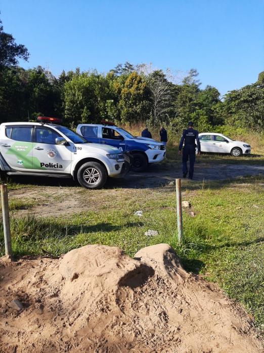 Em primeiro plano areia e ao fundo viaturas estacionadas. #paratodosverem