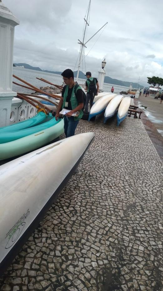 agentes caminham próximo a canoas com bocas viradas para baixo na ponta da praia. #paratodosverem