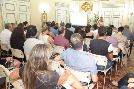 Reunião no salão nobre, com espaço lotado. Há uma pessoa no fundo falando a todos. #Paratodosverem