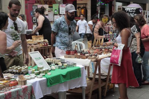 Estandes com objetos expostos em rua. Pessoas circulam pelo local 