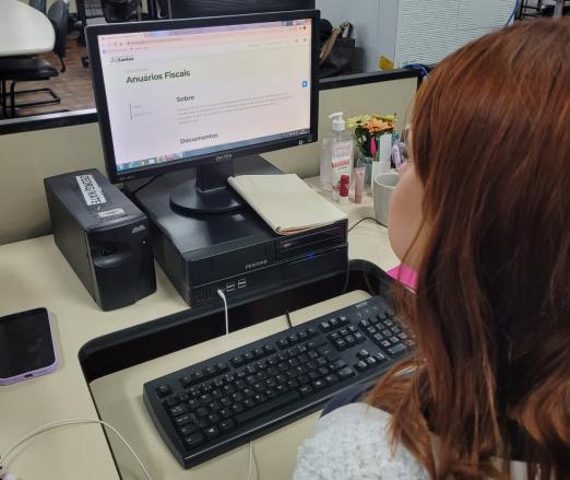 jovem olha computador com anuário #paratodosverem
