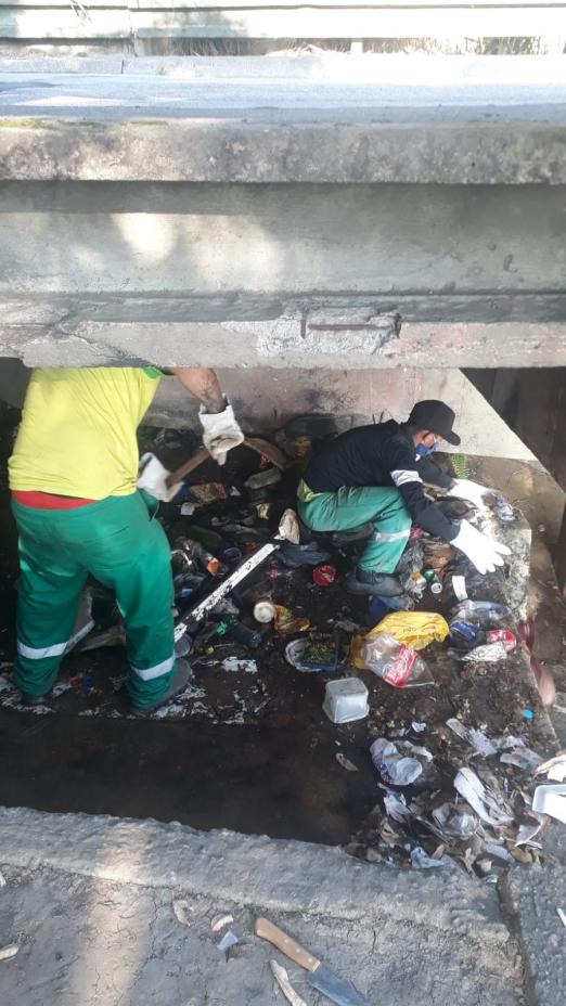 Dois homens limpam local cheio de lixo. #paratodosverem
