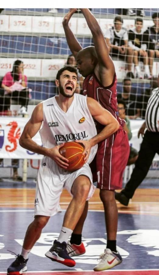 Jogador de basquete segurando a bola na partida e sendo marcado #paratodosverem