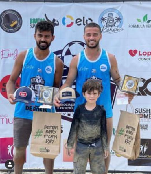 Dois atleta com troféus no pódio e criança na frente #paratodosverem