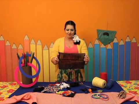 Camila Genaro está em pé em um ambiente multicolorido, rodeada de várias peças artesanais. #Pracegover