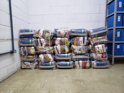 Várias cestas básicas em sacos plásticos estão empilhadas no chão. #Paratodosverem
